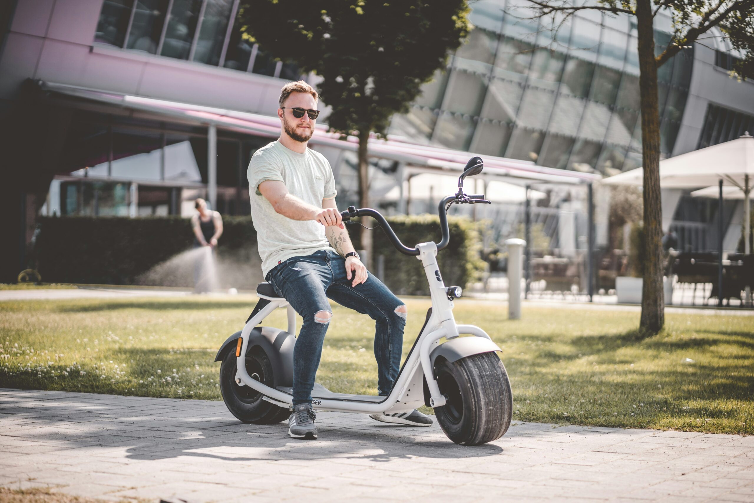 Homem sentado em uma scooter elétrica de pneus largos em ambiente urbano.
