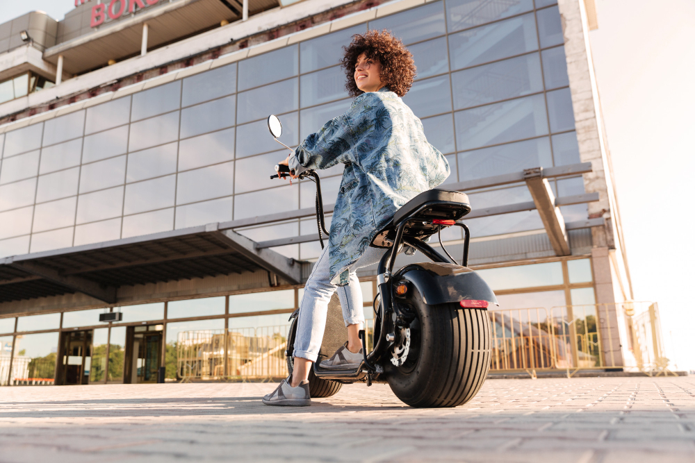  Mulher com expressão confiante sobre uma scooter elétrica robusta em frente a um prédio, sugerindo a questão: scooter elétrica pode andar na rodovia com segurança?