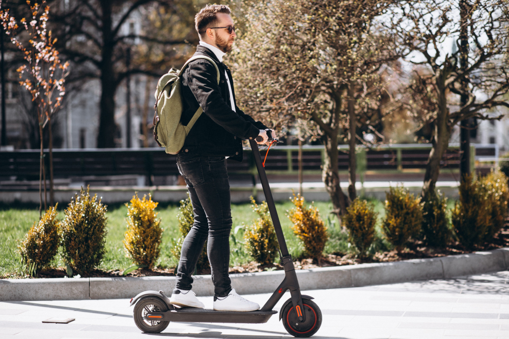 Pessoa em patinete elétrico em área urbana arborizada – patinetes como solução moderna de transportes não poluentes.