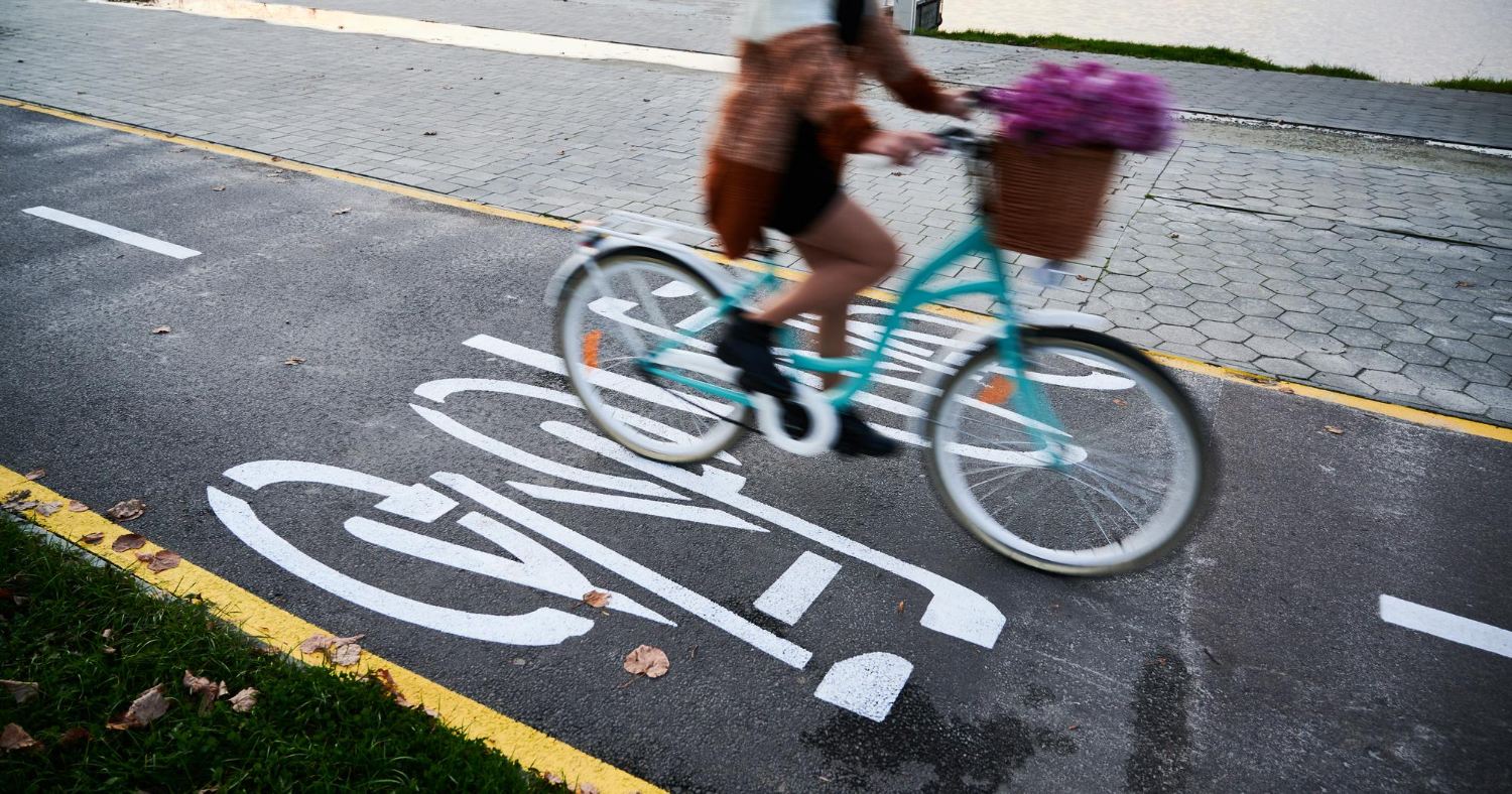 Mulher pedalando em ciclovia e ciclofaixa sinalizada, promovendo mobilidade urbana sustentável. 