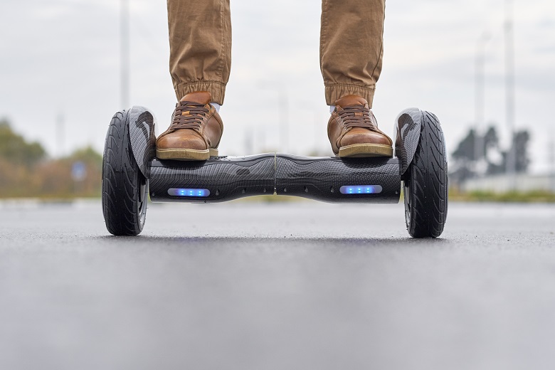 Close up of man using hoverboard on asphalt road. Feet on electrical scooter outdoor, front view