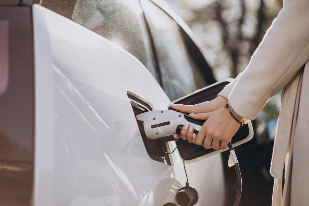 Mulher conectando cabo em carro elétrico para recarregar.