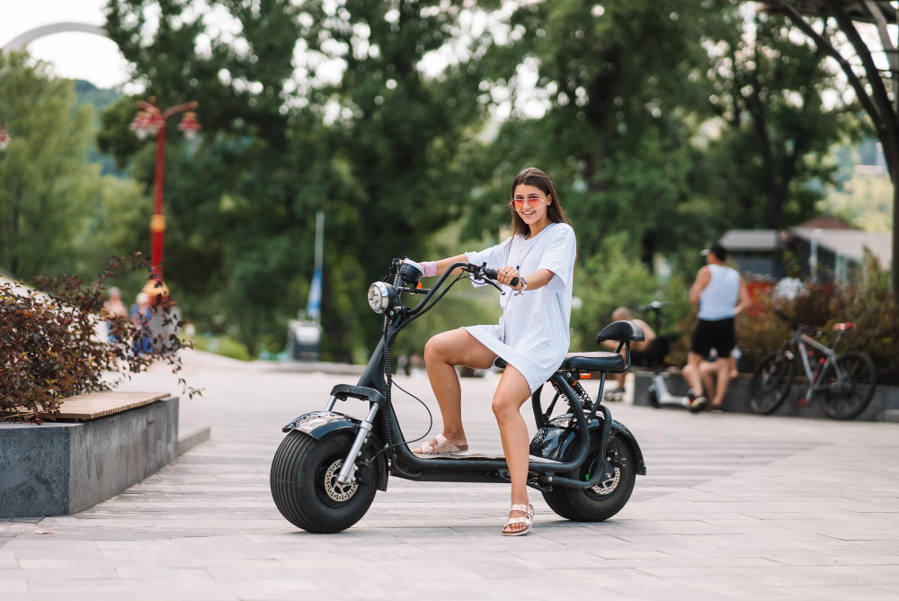 Mulher sorridente pilotando uma moto elétrica em área de lazer ao ar livre durante o dia.